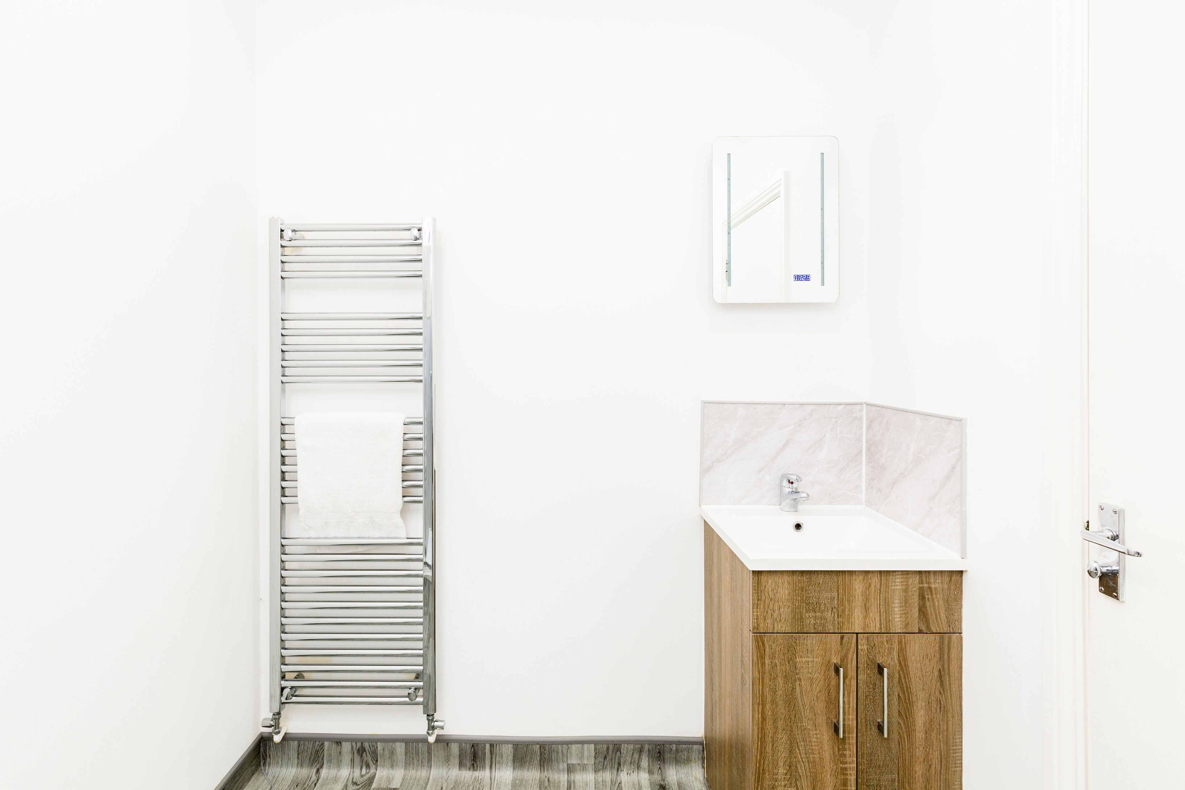A bathroom with a towel rack, a mirror, and a wooden cabinet with a sink.
