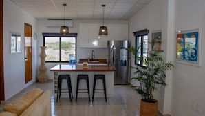 Una cocina moderna con una isla central, taburetes de bar, un refrigerador y una planta en maceta.