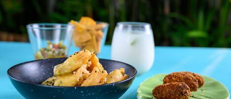 A table with a blue bowl filled with fried snacks, a glass of milk, and a plate with cookies.