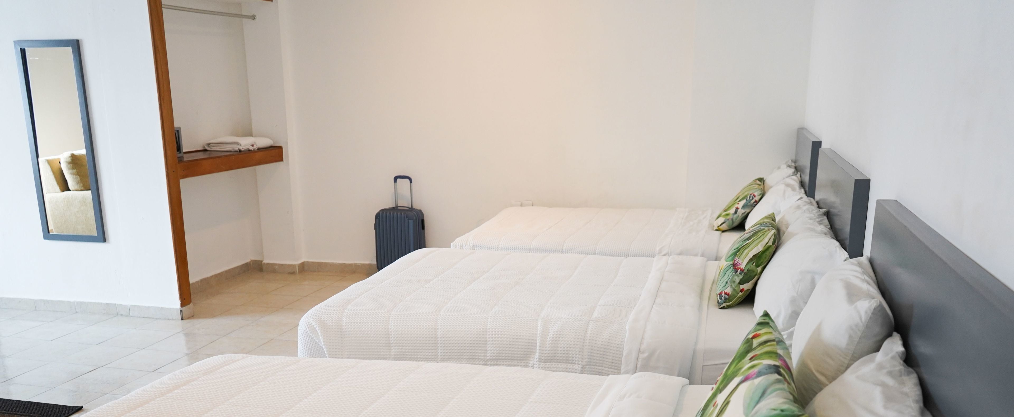 Una habitación de hotel con dos camas, una maleta, un espejo y un estante con toallas dobladas.