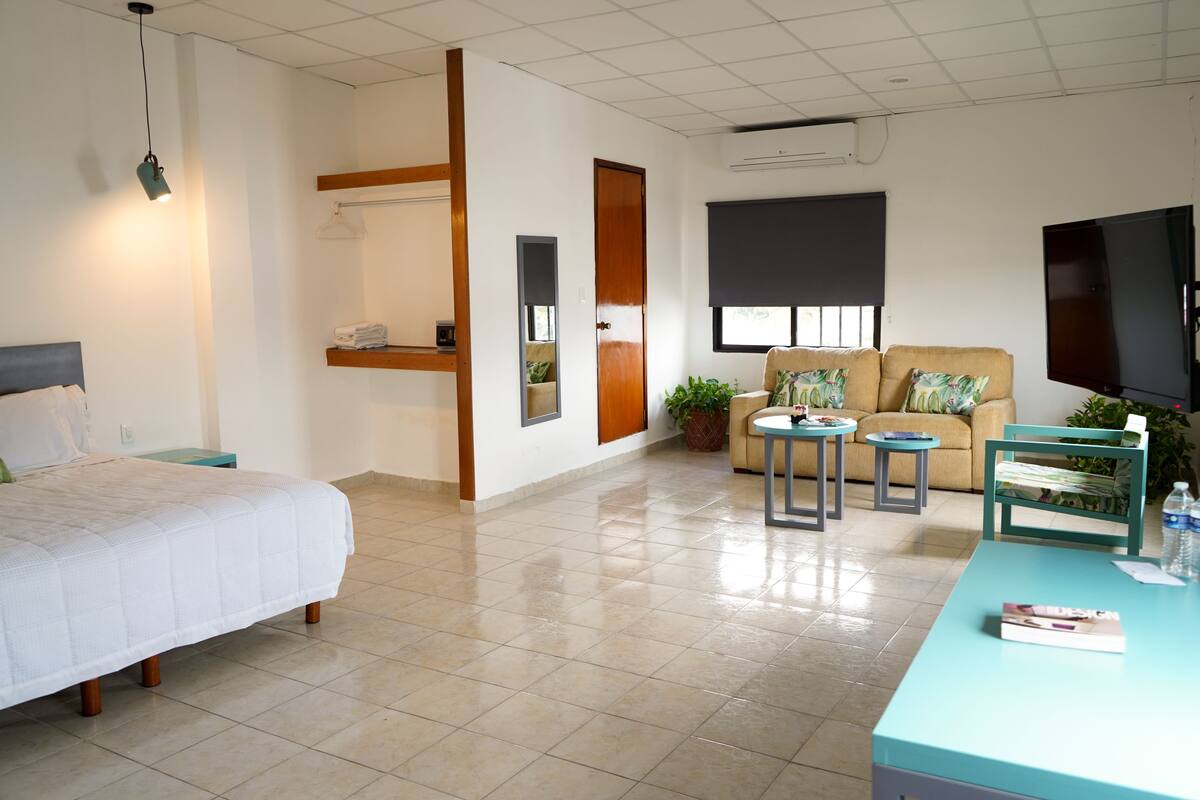 A hotel room with a bed, a sofa, a small table, a TV, and a window.