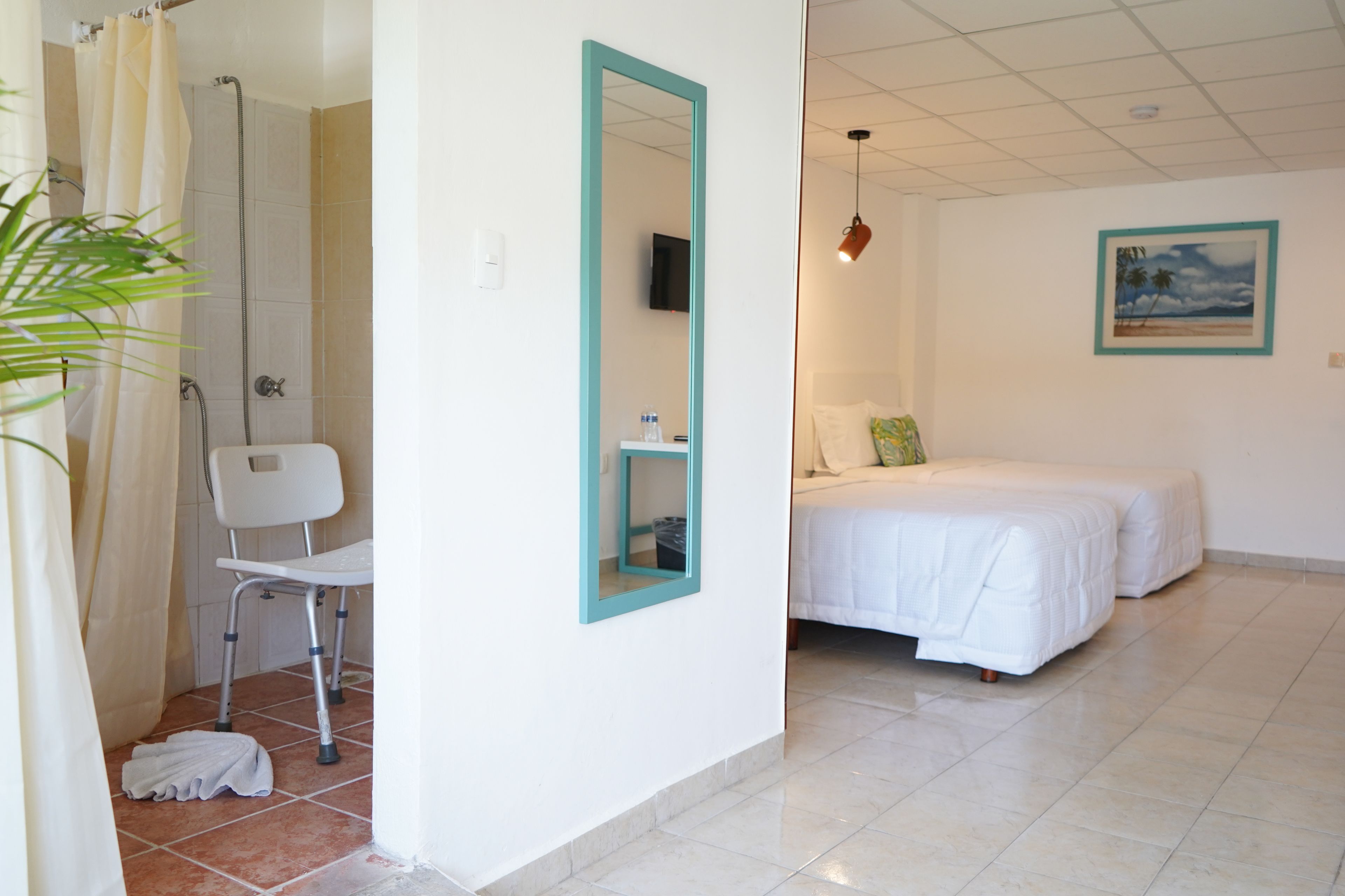A hotel room with a shower, a bed, a chair, and a mirror.