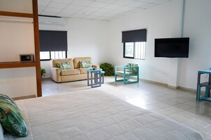 Uma sala de estar ampla com sofá, uma mesinha, televisão na parede e uma janela com persiana.