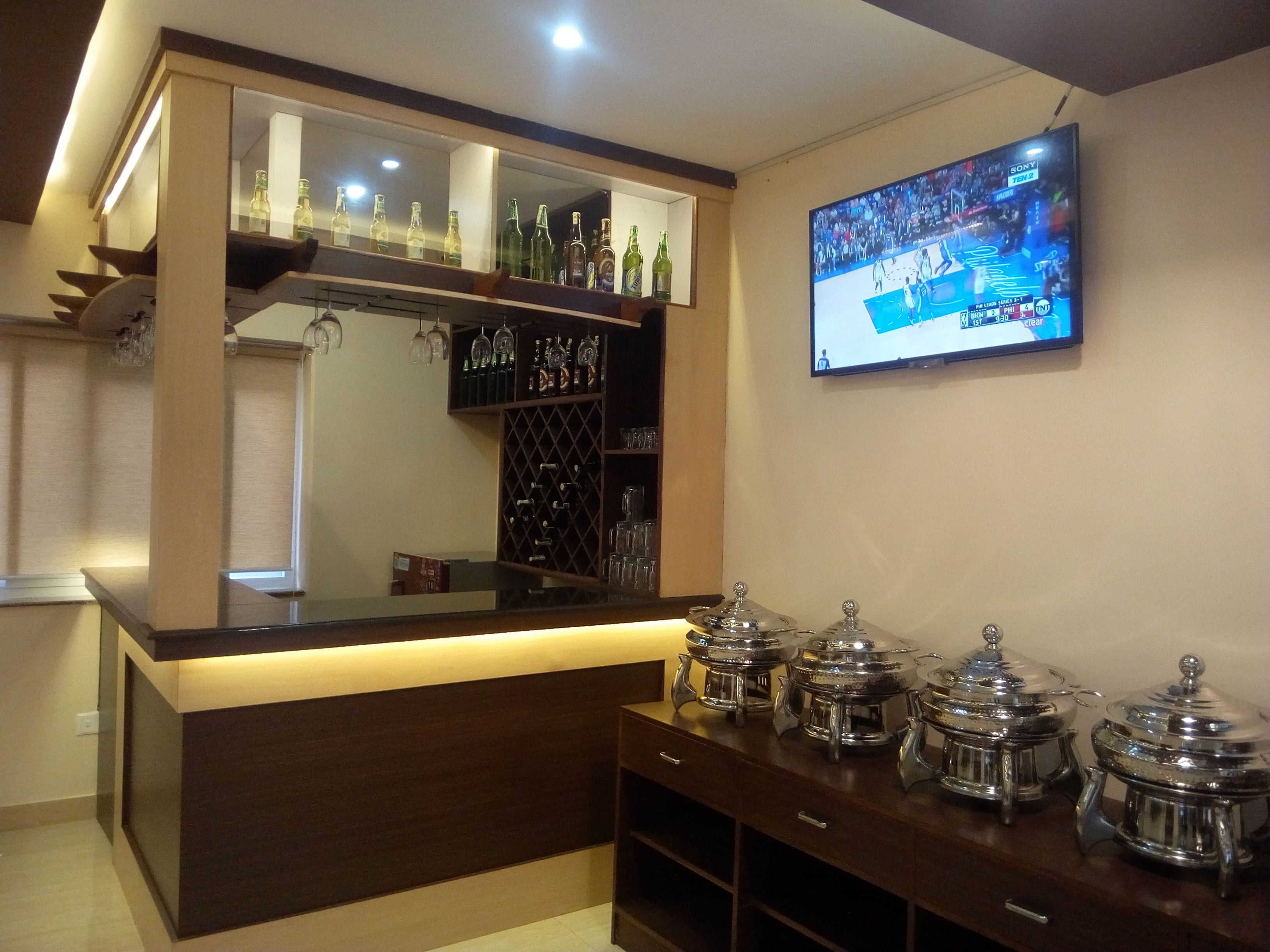 A bar area with a counter, wine bottles, glasses, and a TV displaying a sports event.