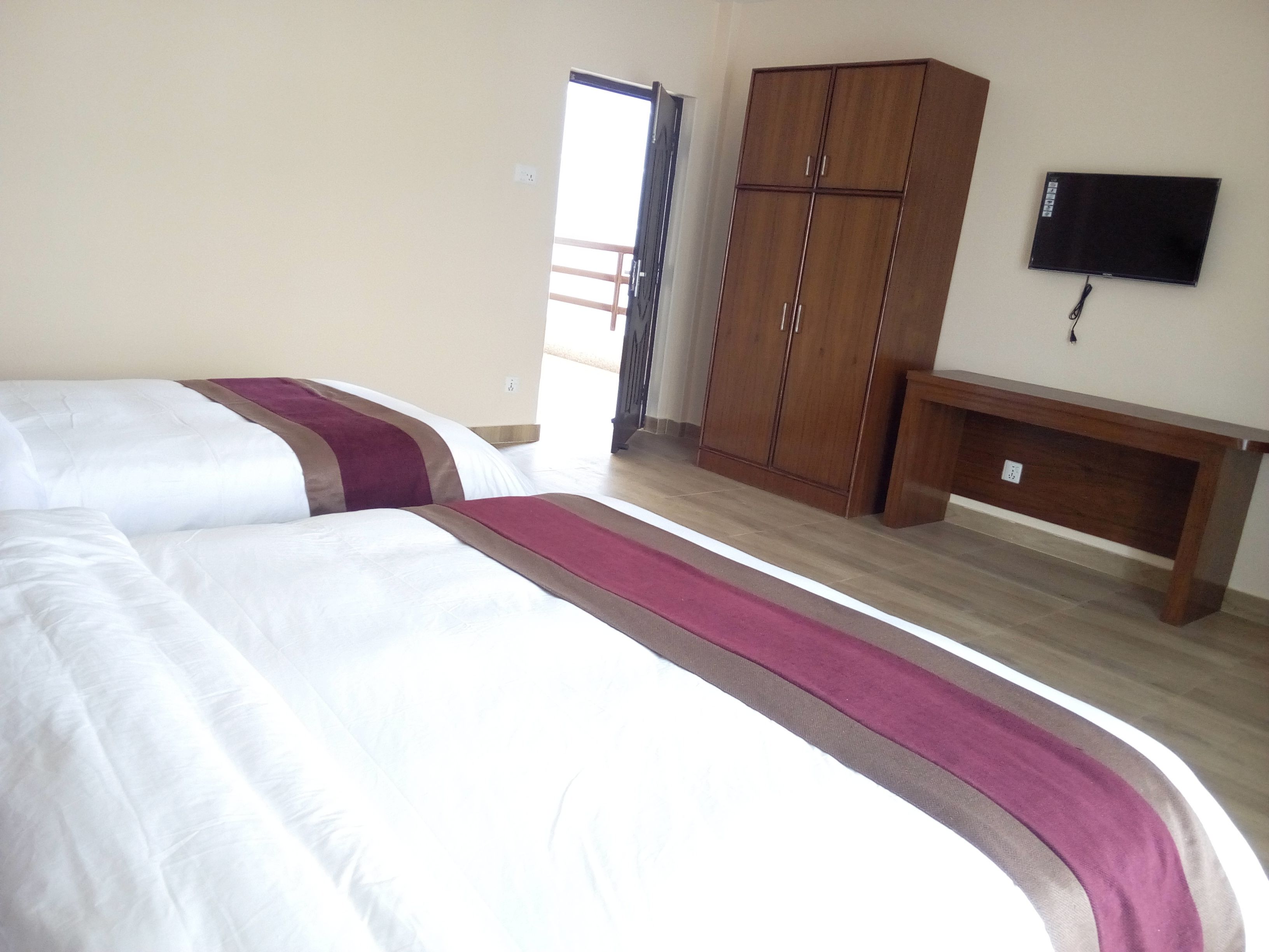 A hotel room with two beds, a wardrobe, a TV, and a bench.