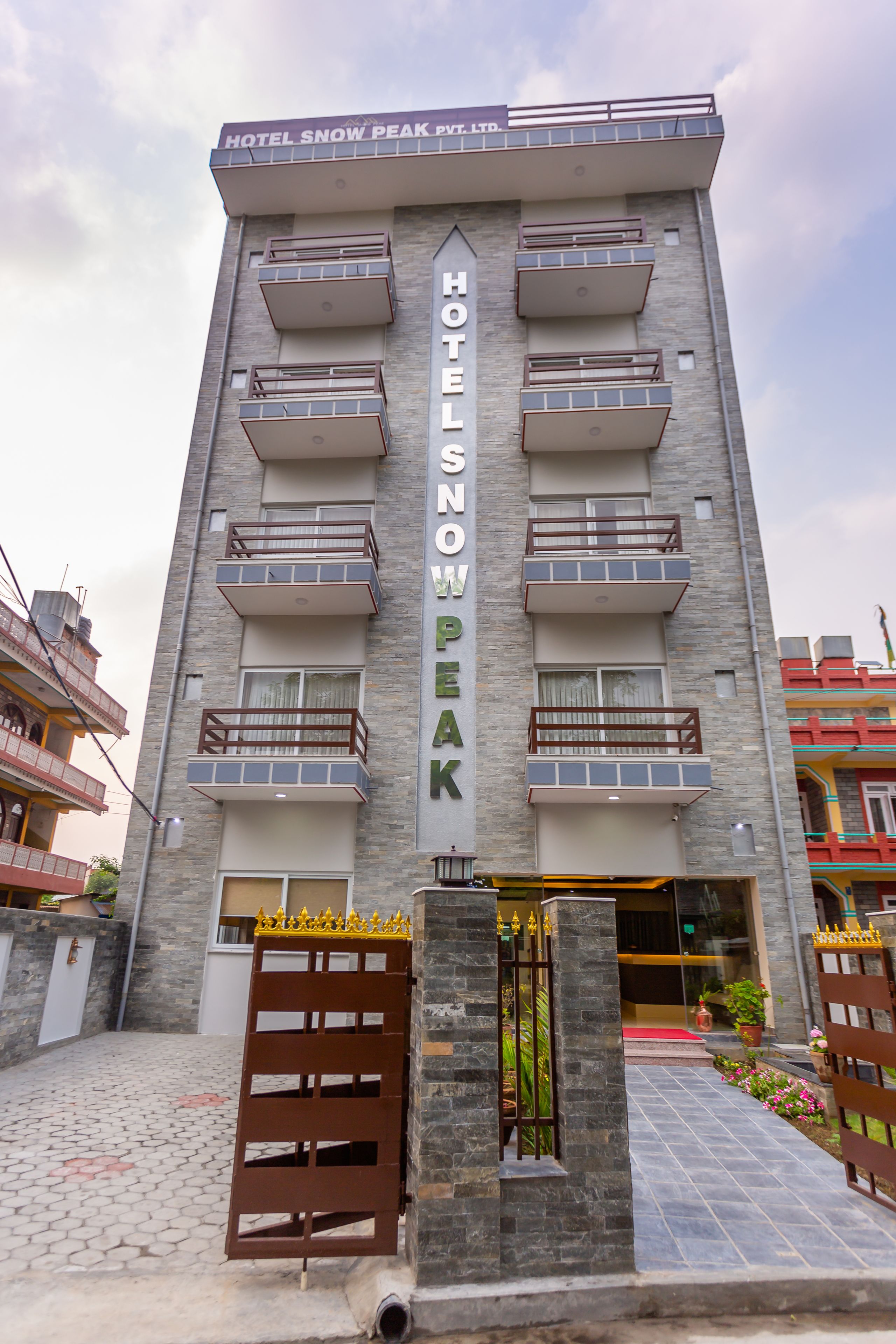Un hotel de varios pisos con balcones, un cartel llamativo que dice "HOTEL SNOW PEAK" y una entrada con portones.