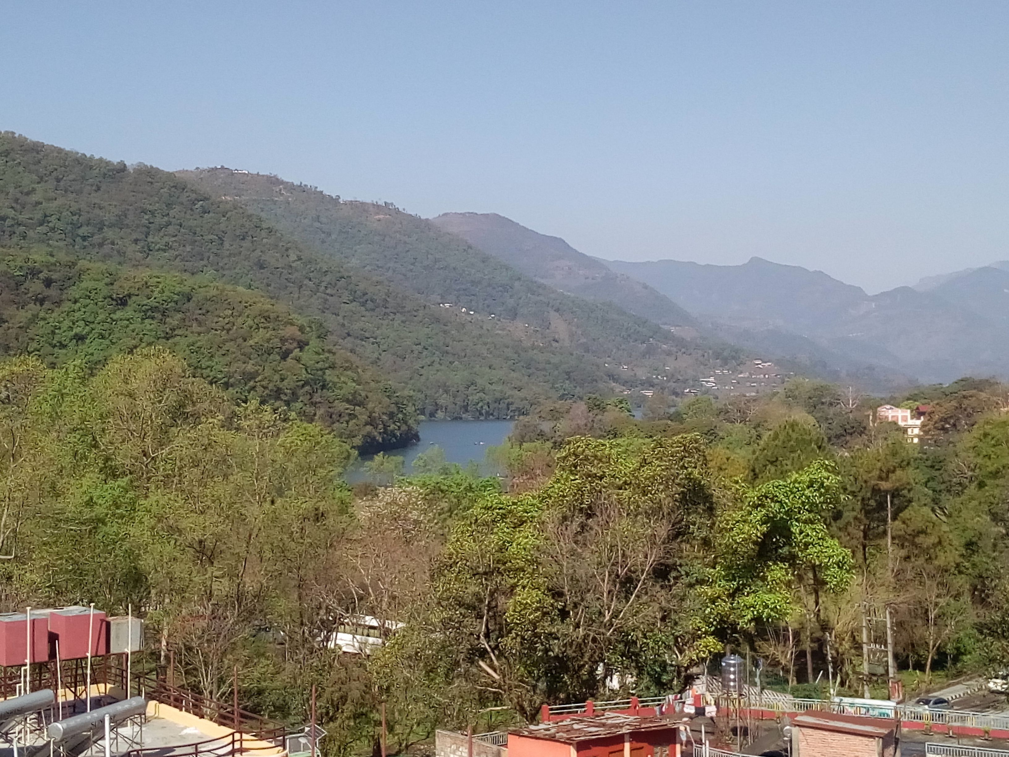 Paisaje montañoso con un lago, rodeado de un bosque denso y edificios dispersos.