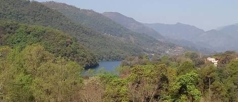 Paisaje montañoso con un lago, rodeado de un bosque denso y edificios dispersos.