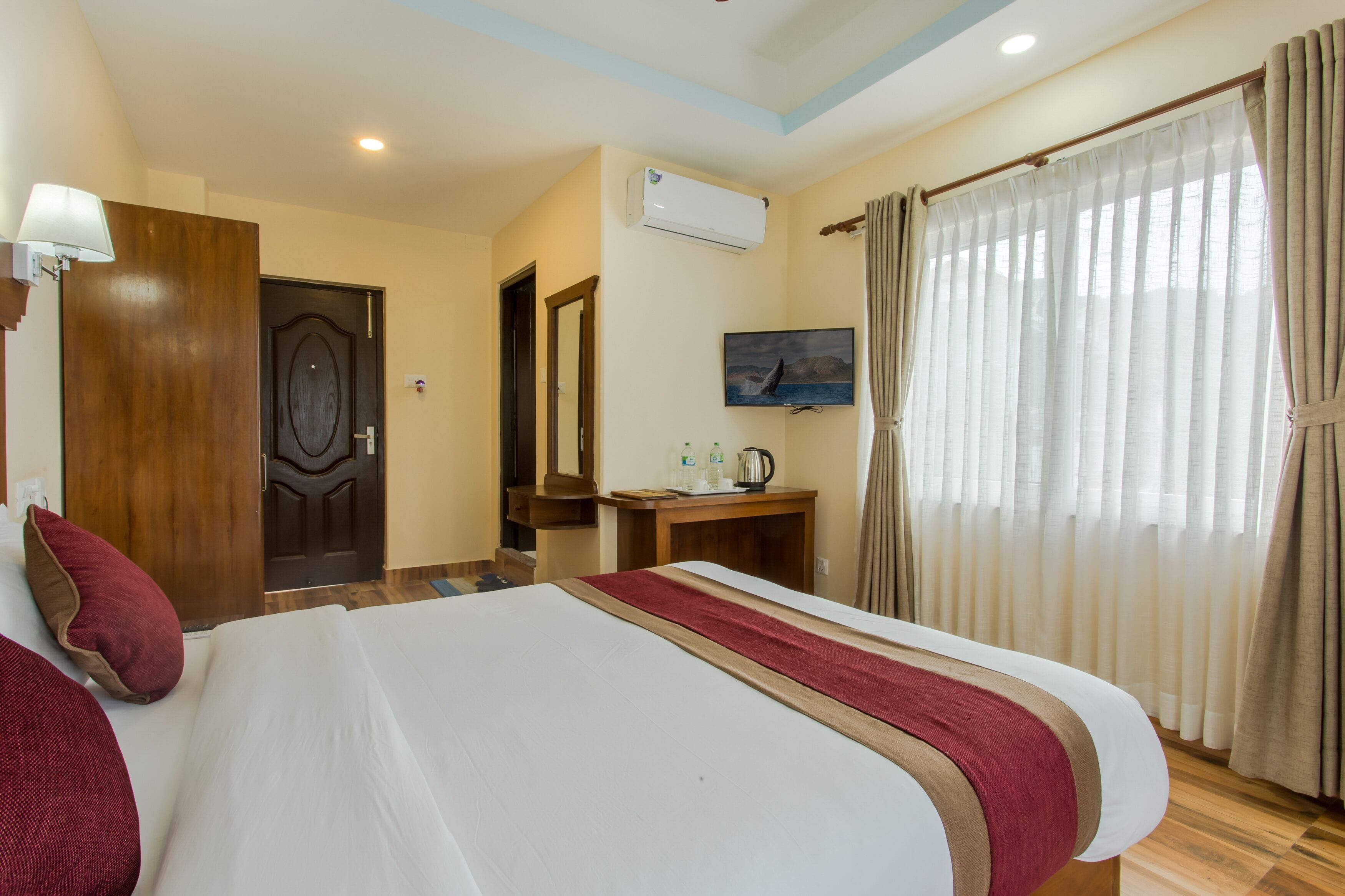 A hotel room with a large bed, a wooden desk, a television, and a window with curtains.