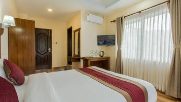 A hotel room with a large bed, a wooden desk, a television, and a window with curtains.