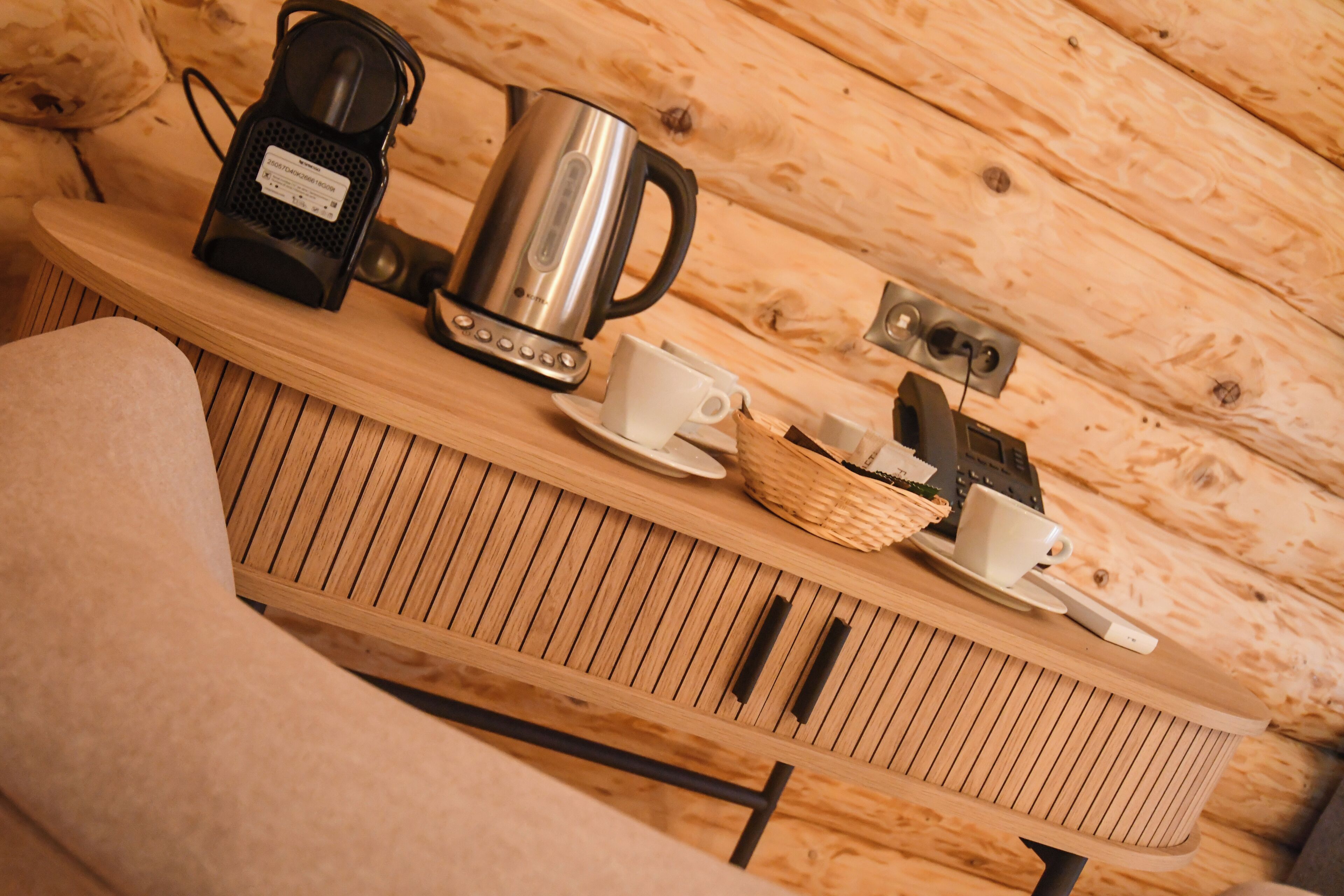 A wooden table with a kettle, a coffee maker, and a cup on a wooden wall.