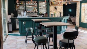 A bar area with a green bar counter, multiple stools, and a variety of bottles and glasses.