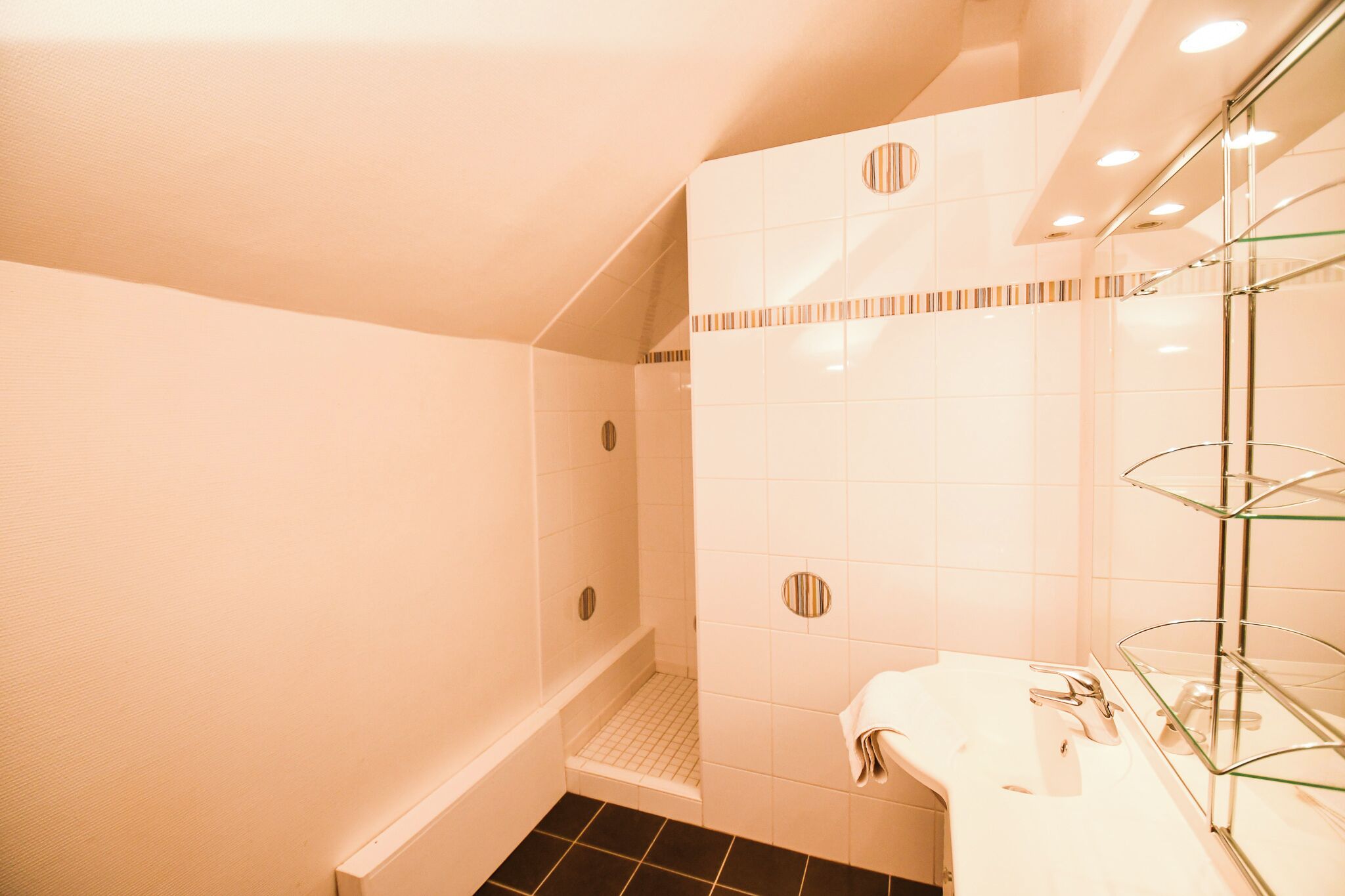 Un baño moderno con ducha, un lavabo con estante de vidrio y pared de azulejos con diseños circulares.