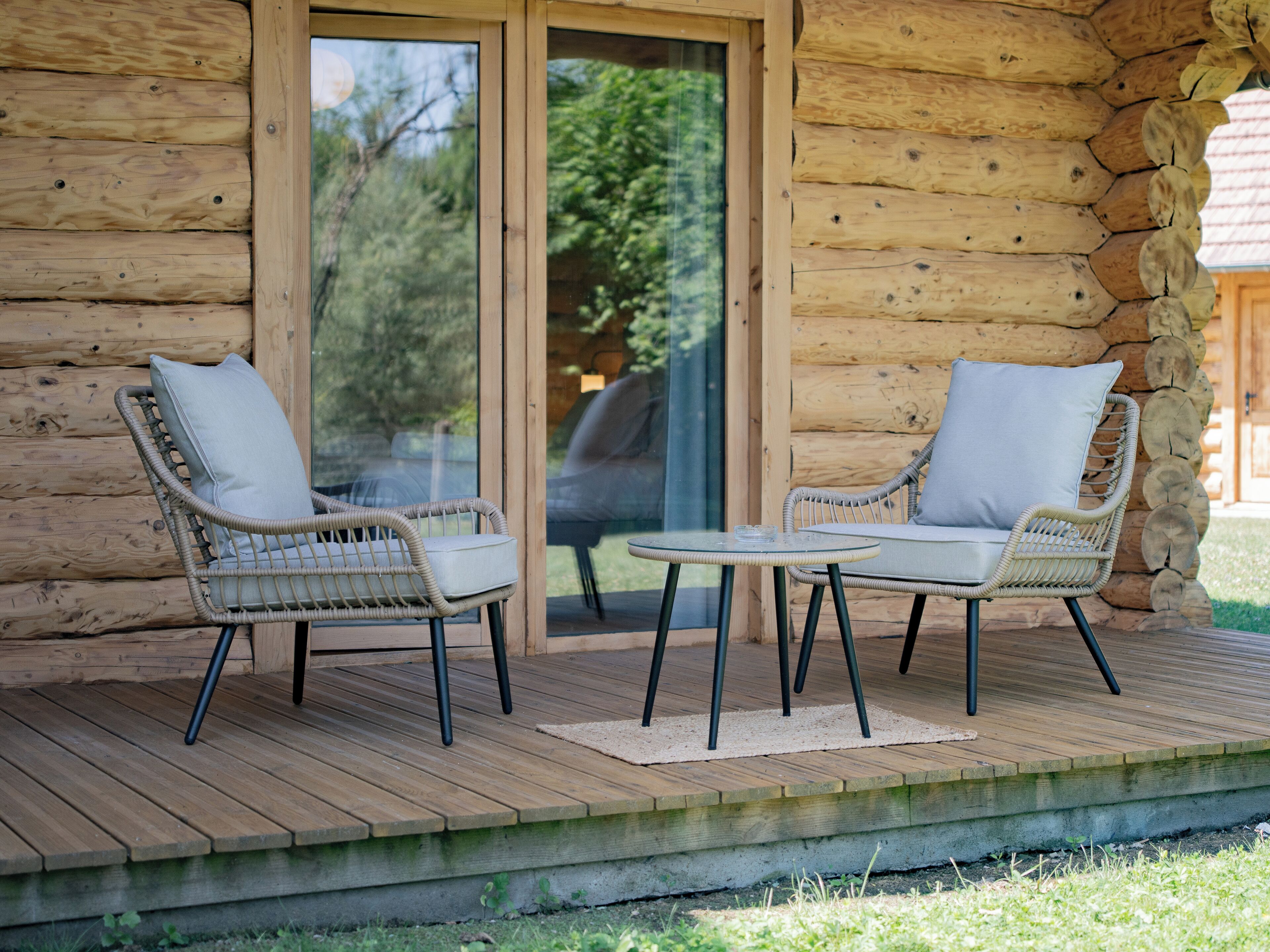 Una cabaña de troncos de madera con dos sillas de mimbre y una pequeña mesa en una terraza de madera.