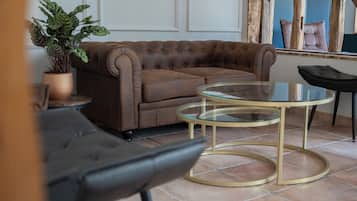 A brown leather sofa, a glass coffee table with gold legs, and a black armchair in a room with tiled flooring.