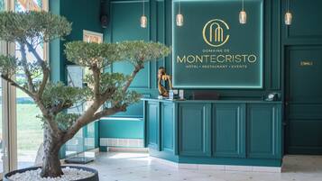 A reception desk with a sign for Domaine de Montecristo hotel, featuring a modern design with teal walls and hanging pendant lights.