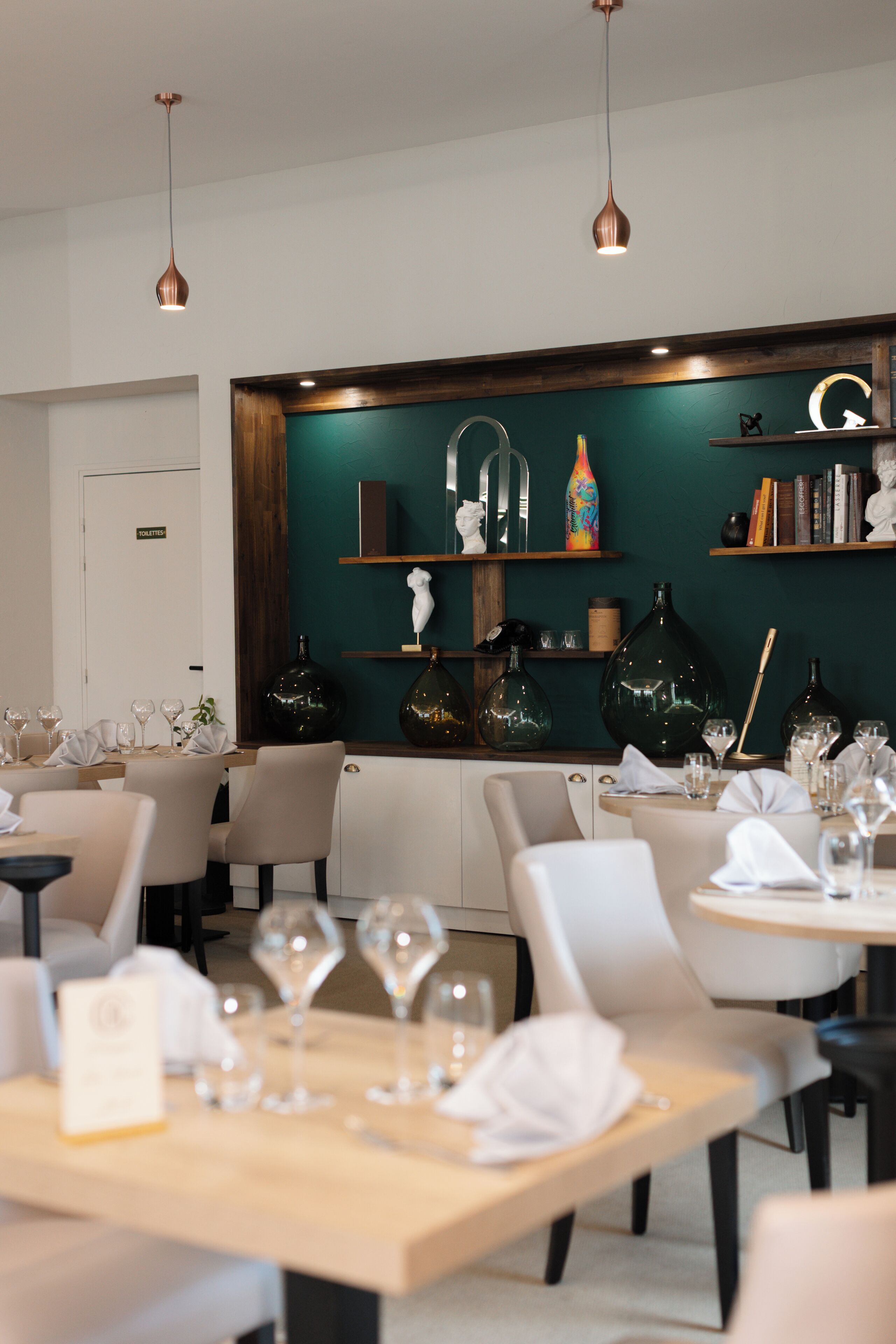 A restaurant with tables set for dining, a green accent wall, and pendant lighting.