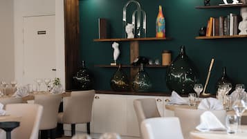 A restaurant with tables set for dining, a green accent wall, and pendant lighting.