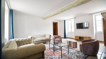 A living room with a sofa, armchairs, a coffee table, and a TV on the wall.