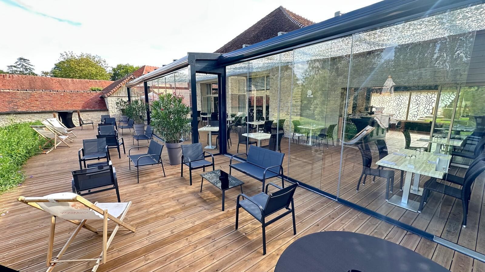 A covered outdoor patio with wooden flooring, black chairs, and tables.