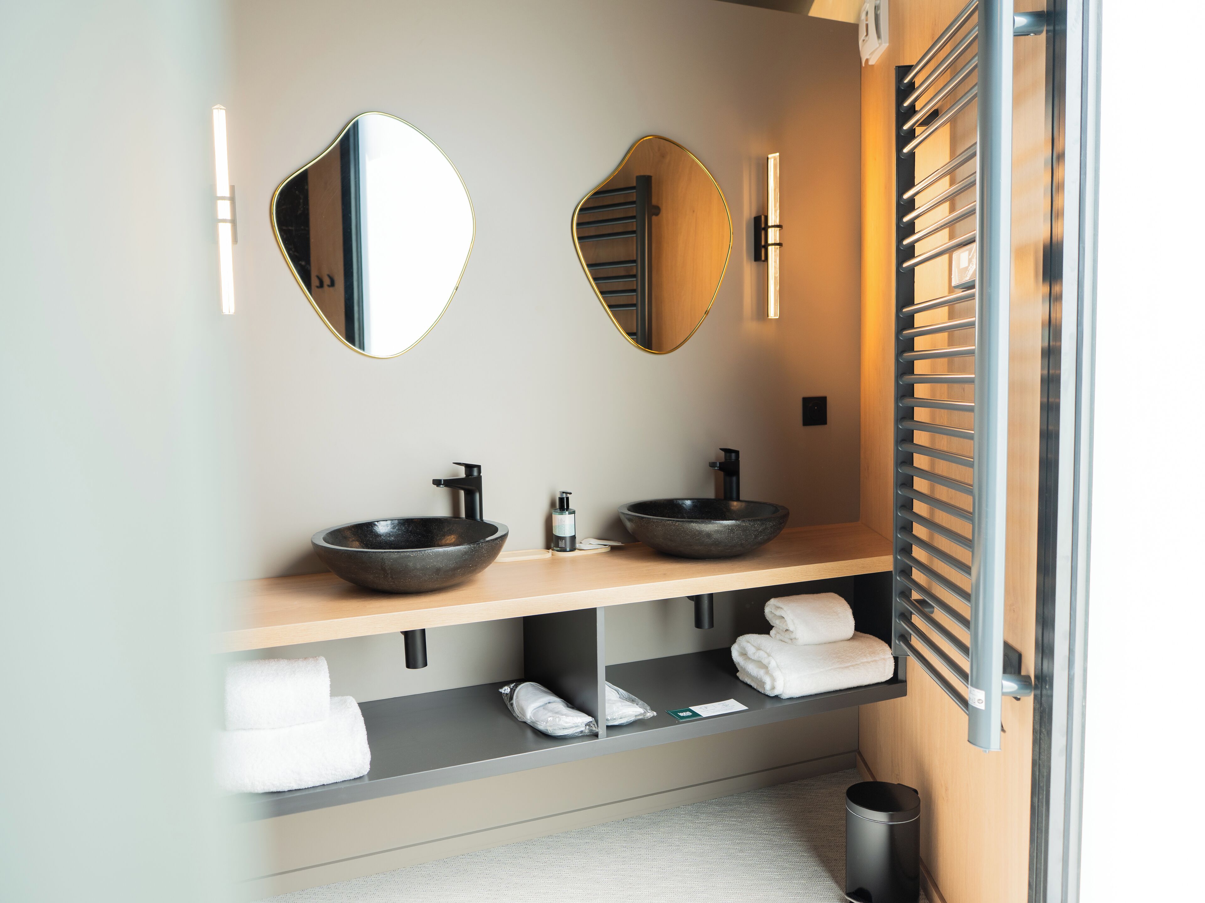 Un baño moderno con dos lavamanos tipo recipiente, un espejo grande y un perchero para toallas.