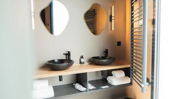 Un baño moderno con dos lavamanos tipo recipiente, un espejo grande y un perchero para toallas.