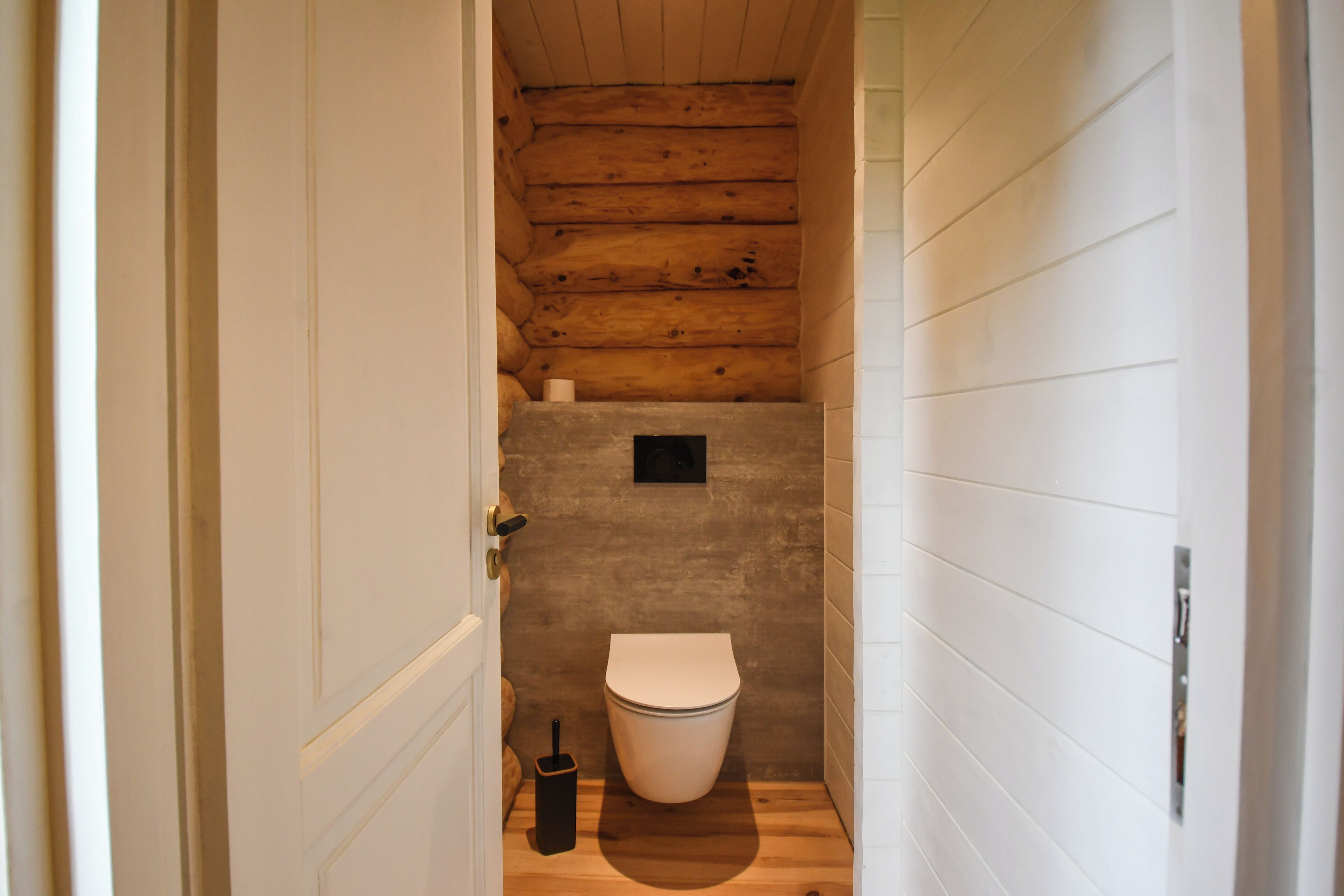 Une petite salle de bain aux murs lambrissés, avec des toilettes blanches, une petite poubelle et un seul luminaire au plafond.
