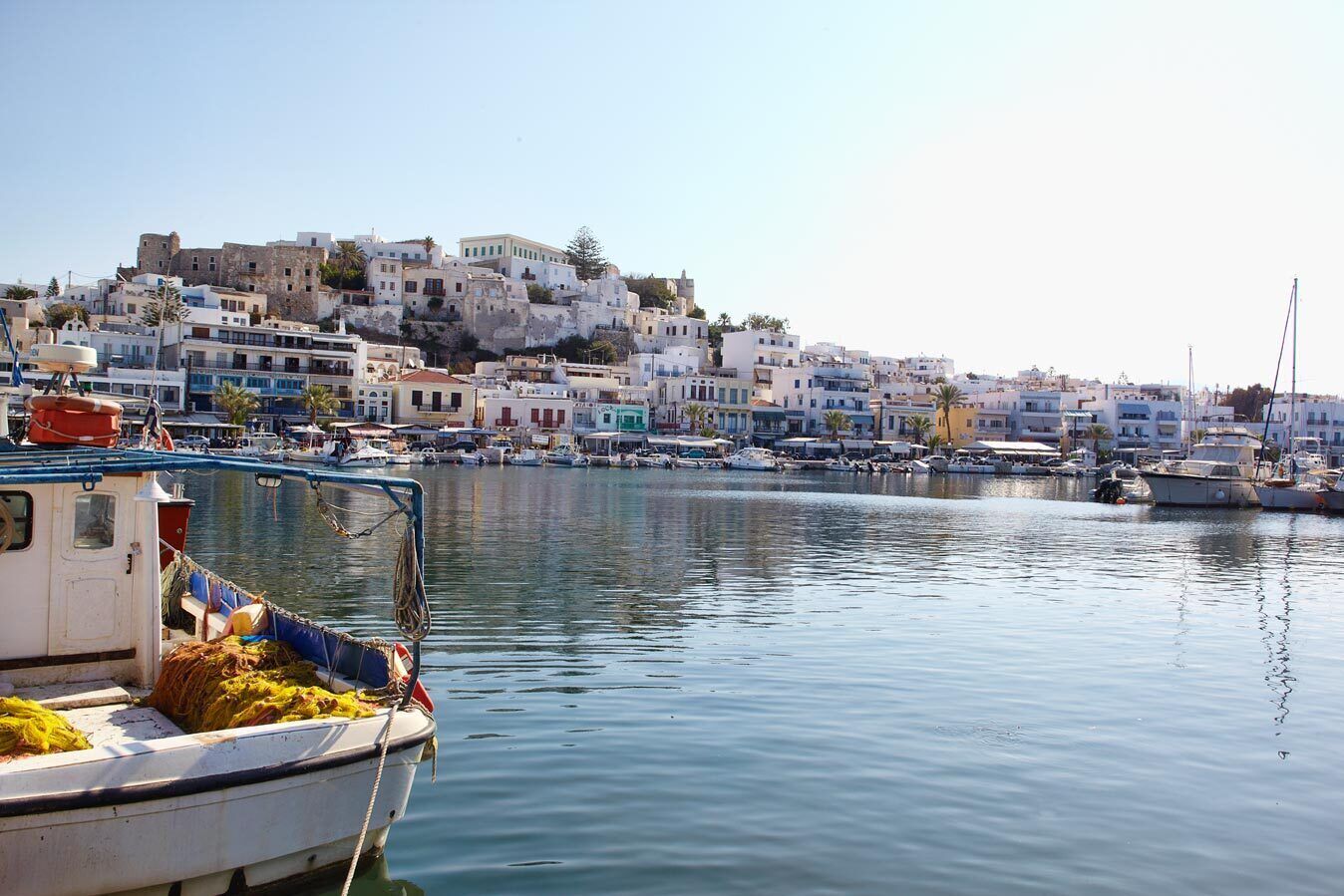 A coastal town with white buildings, a marina with boats, and a clear sky.