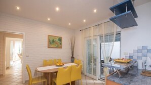 A modern kitchen with a dining area, featuring a white brick wall, a painting, and a sliding glass door leading to a balcony. - Apartment Mia (Opatija)