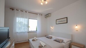 A bedroom with a bed, a TV, a window with curtains, and wall-mounted lights. - Apartment Mia (Opatija)
