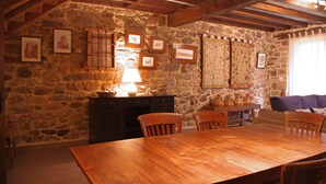 A rustic stone wall with framed pictures, a wooden table with chairs, and a lamp. - THE CORNER OF BESAYA. A mountain house in the Saja-Besaya reserve (Villasuso de Cieza)