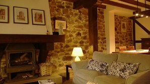 A cozy living room with a stone wall, a fireplace, a sofa, and a dining area. - THE CORNER OF BESAYA. A mountain house in the Saja-Besaya reserve (Villasuso de Cieza)