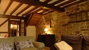 A cozy living room with a stone wall, wooden beams, a fireplace, and two sofas with patterned cushions. - THE CORNER OF BESAYA. A mountain house in the Saja-Besaya reserve (Villasuso de Cieza)