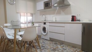 A modern kitchen with a microwave, washing machine, and a compact refrigerator. There is a dining table with chairs and a patterned floor. - LOFT CELINDA CORDOBA ESTACION (Córdoba)