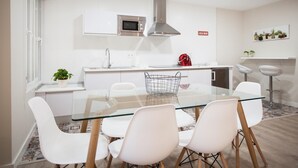 A modern kitchen with white cabinets, a stainless steel microwave, and a red kettle. There is a glass dining table with white chairs and a metal basket. - LOFT CELINDA CORDOBA ESTACION (Córdoba)