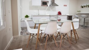 A modern kitchen with white cabinets, a stainless steel range hood, and a glass dining table with four white chairs. - LOFT CELINDA CORDOBA ESTACION (Córdoba)