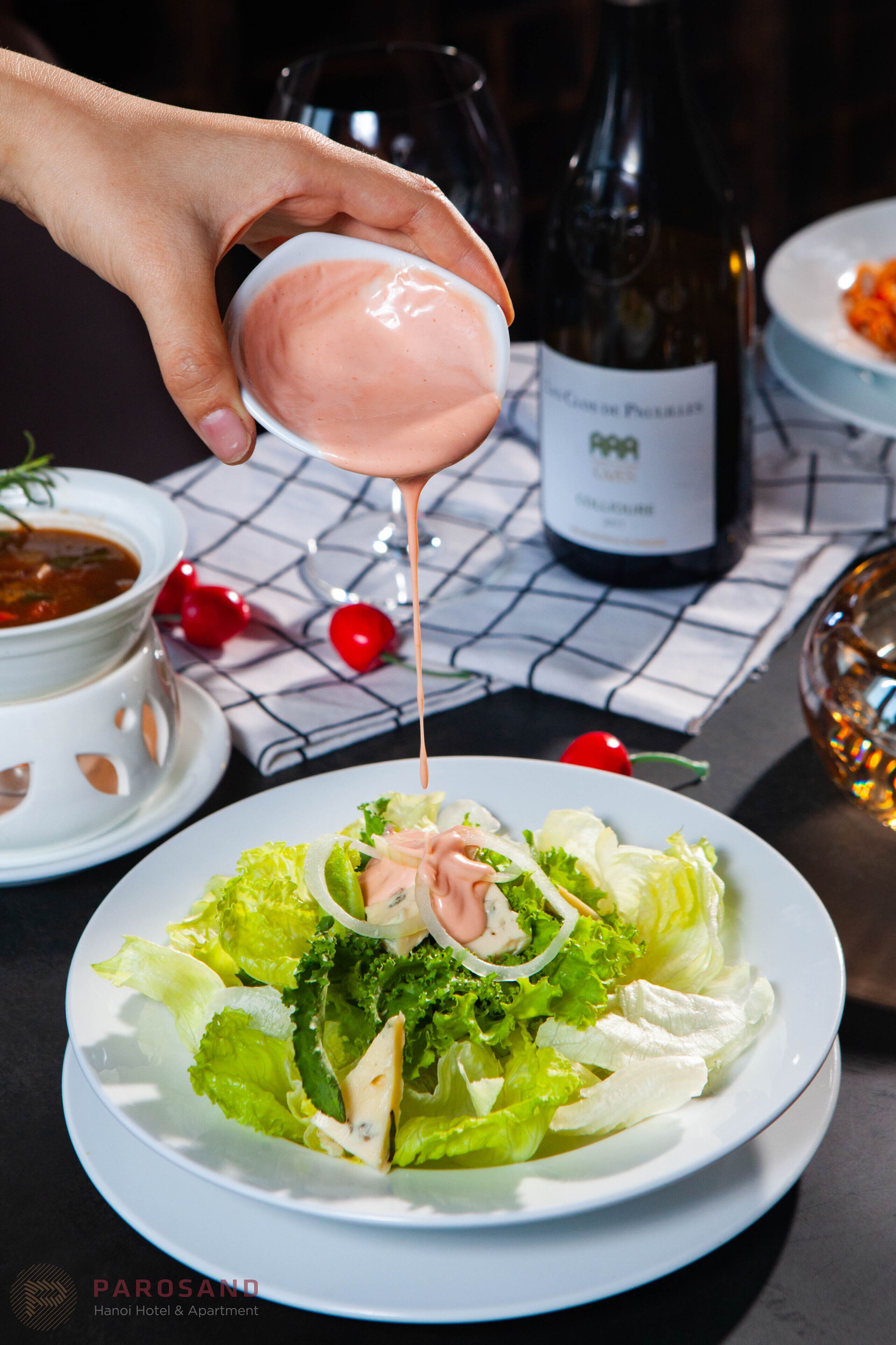 A hand pouring dressing over a salad on a plate.