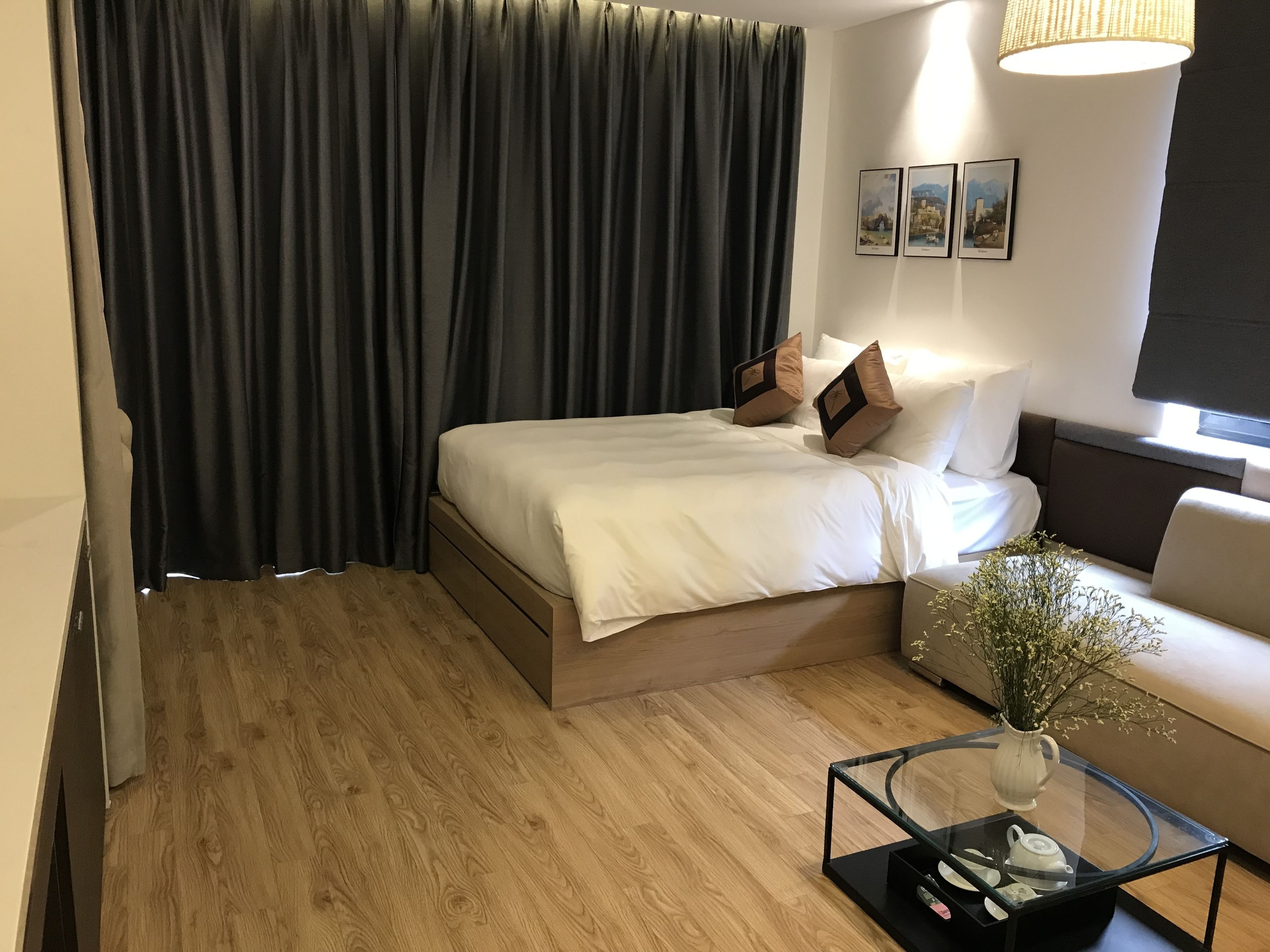 Quarto de hotel moderno com uma cama, uma mesa de centro de vidro, um vaso com flores e um sofá.