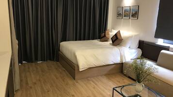 Quarto de hotel moderno com uma cama, uma mesa de centro de vidro, um vaso com flores e um sofá.