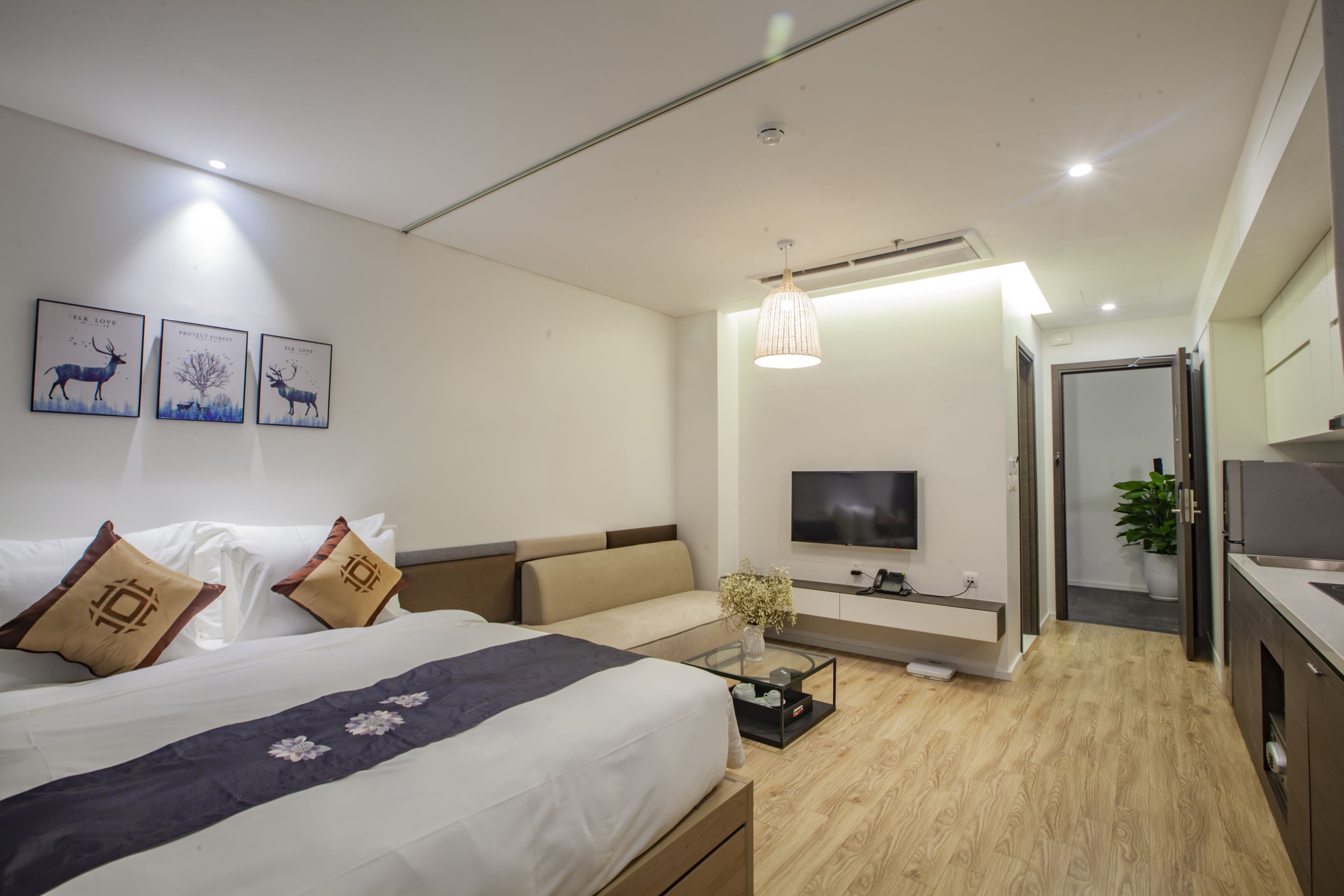 A modern hotel room with a large bed, a TV, a desk, and a bathroom visible through an open door.