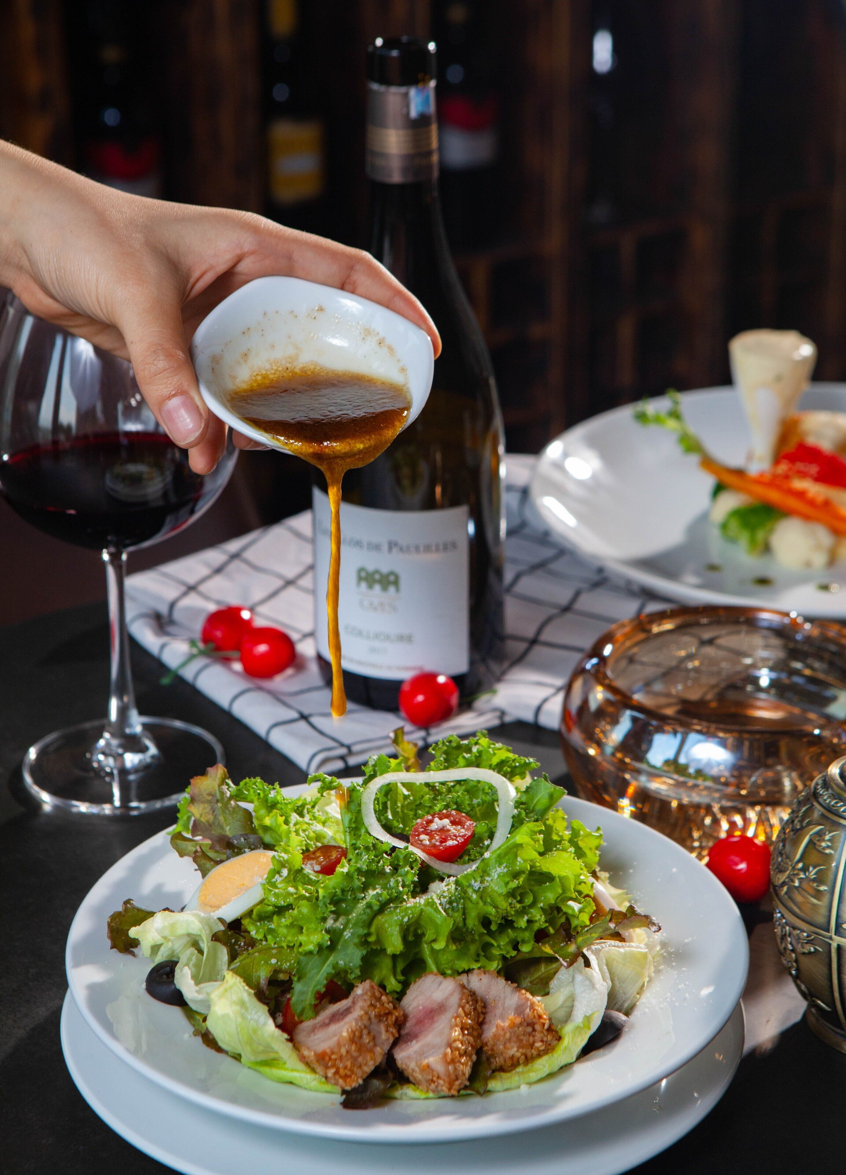 A table with a plate of food, a bottle of wine, and a glass of red wine.
