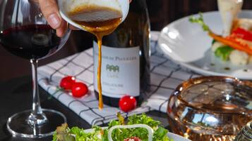 A table with a plate of food, a bottle of wine, and a glass of red wine.
