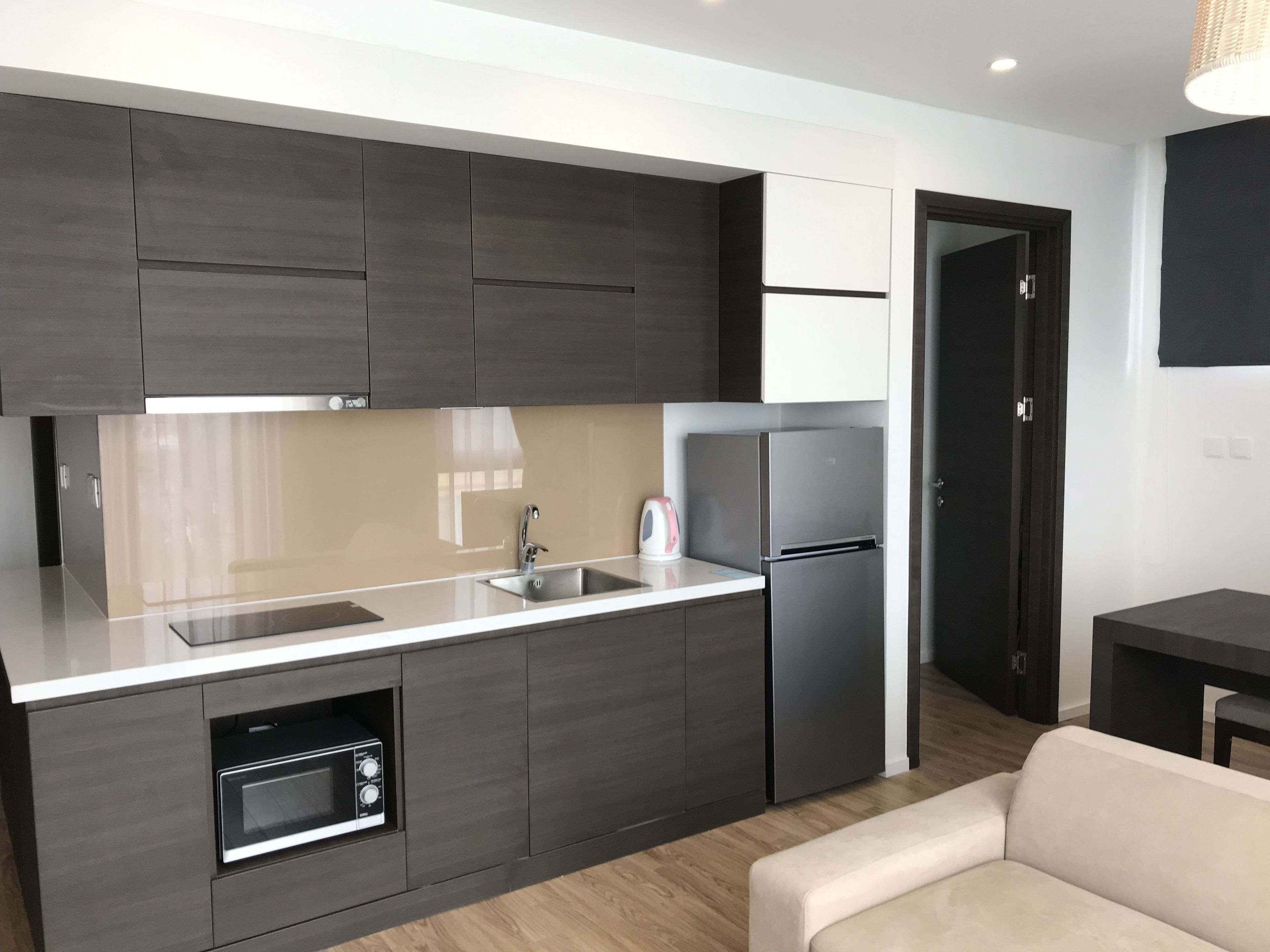 A modern kitchen with dark cabinetry, a stainless steel refrigerator, a built-in oven, and a sink.