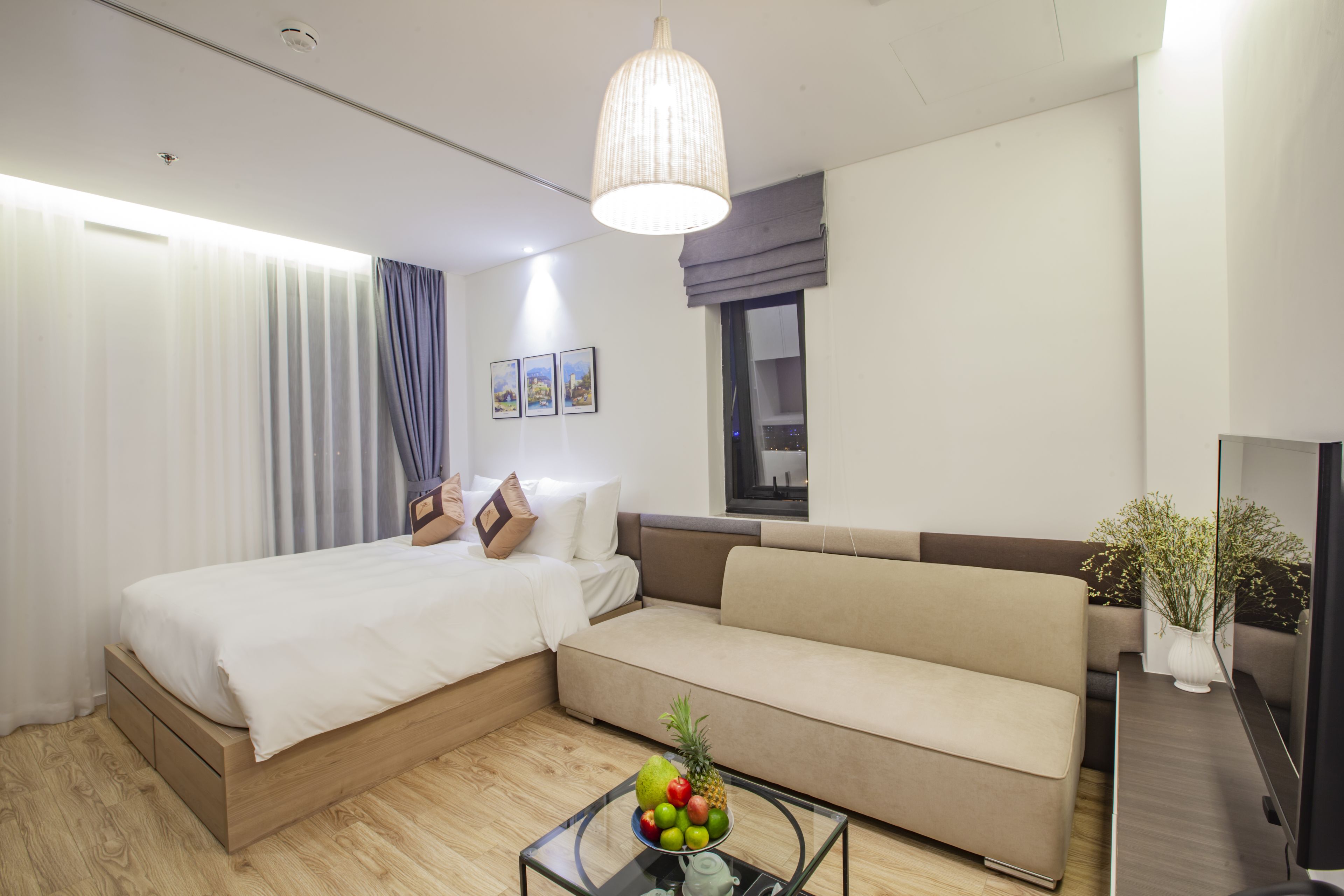 A modern hotel room with a bed, sofa, and a glass coffee table with fruit.