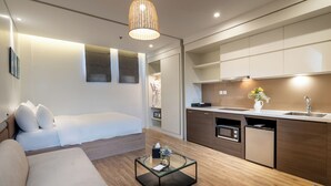 Een moderne, compacte leefruimte met een bank, een glazen salontafel, een kitchenette en een inloopkast.