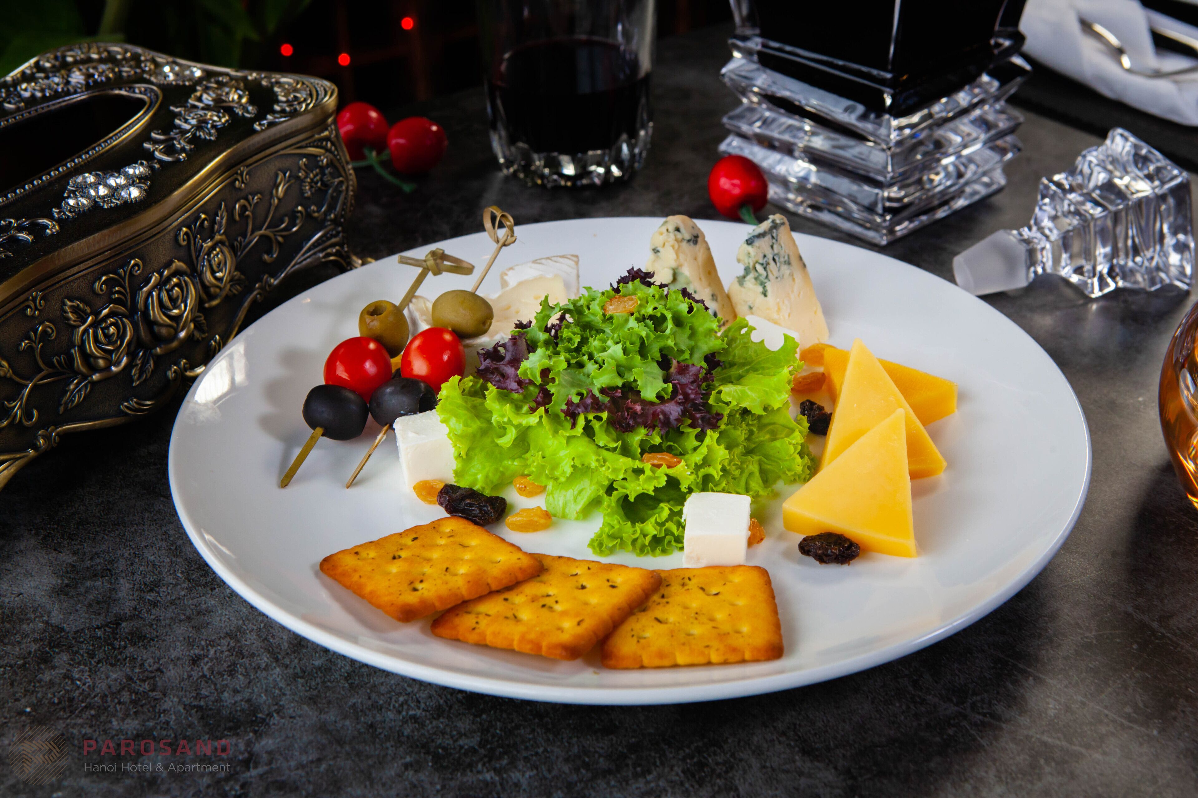A plate with cheese, grapes, olives, and crackers on a table.