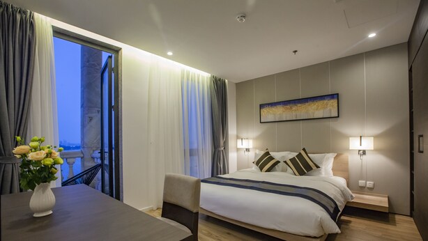 Een hotelkamer met een bed, bedlampjes, een tafeltje met een bloevas en uitzicht op het landschap door een raam.