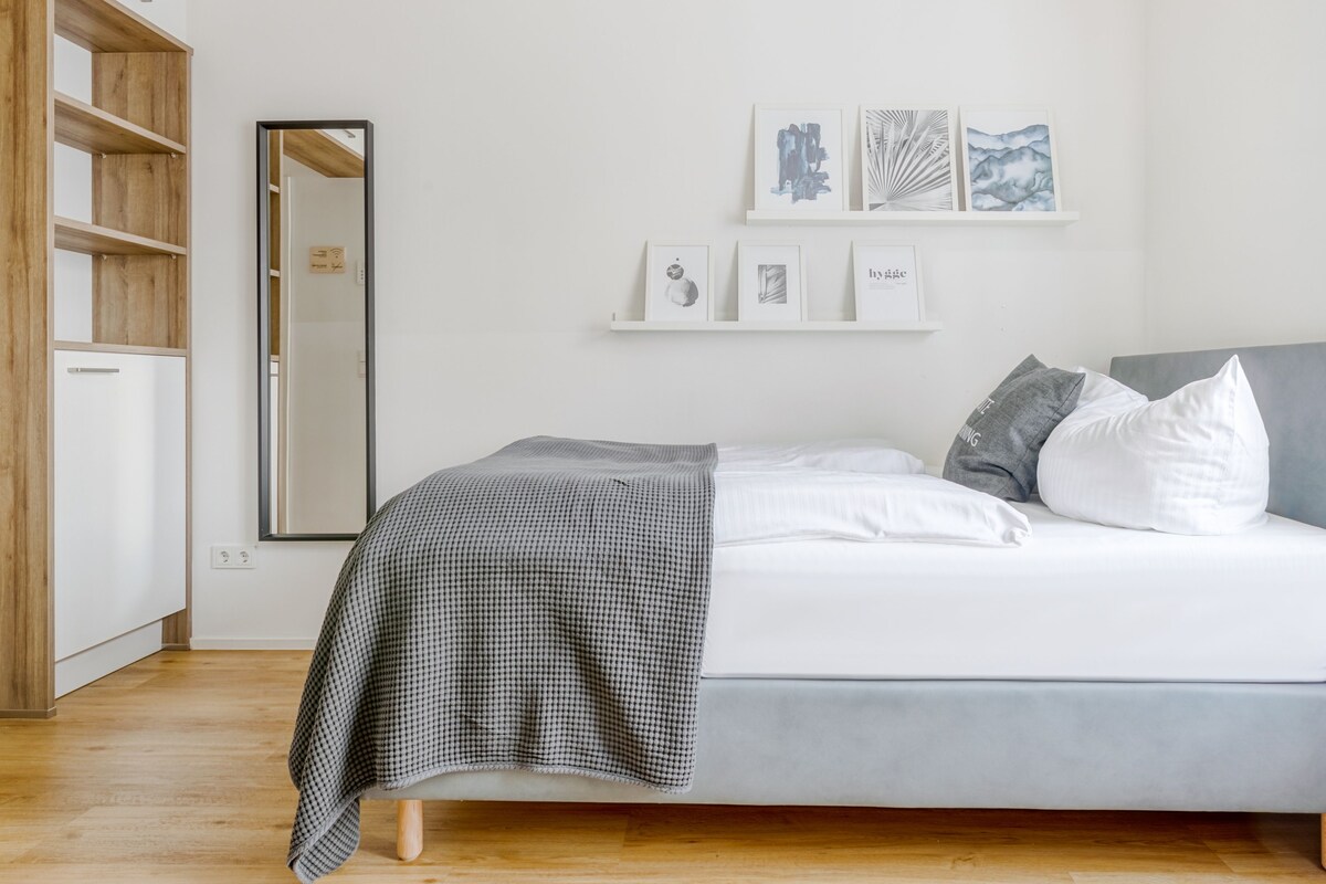 Une chambre à coucher avec un lit, une armoire et un miroir. Trois tableaux encadrés sont accrochés au mur.