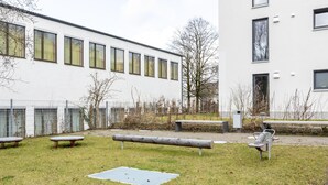 A grassy outdoor area with benches and a metal table, surrounded by a white building with multiple windows. - Limehome Augsburg (Augsburg)