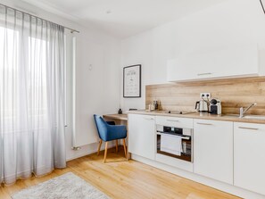 Une cuisine moderne avec des meubles blancs, un plan de travail en bois, une machine à café et une chaise bleue.
